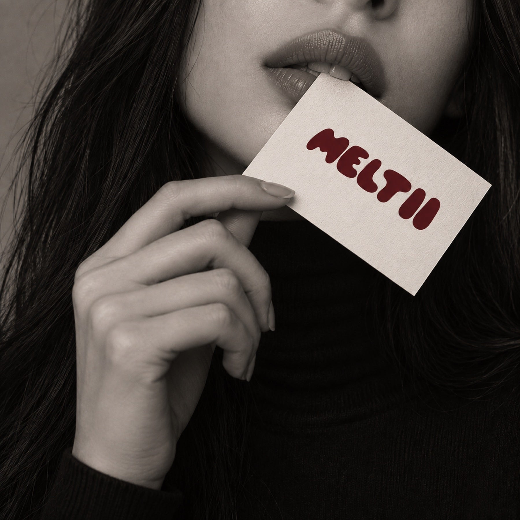 An ivory Meltii card held gently at the lips, photographed in black and white.