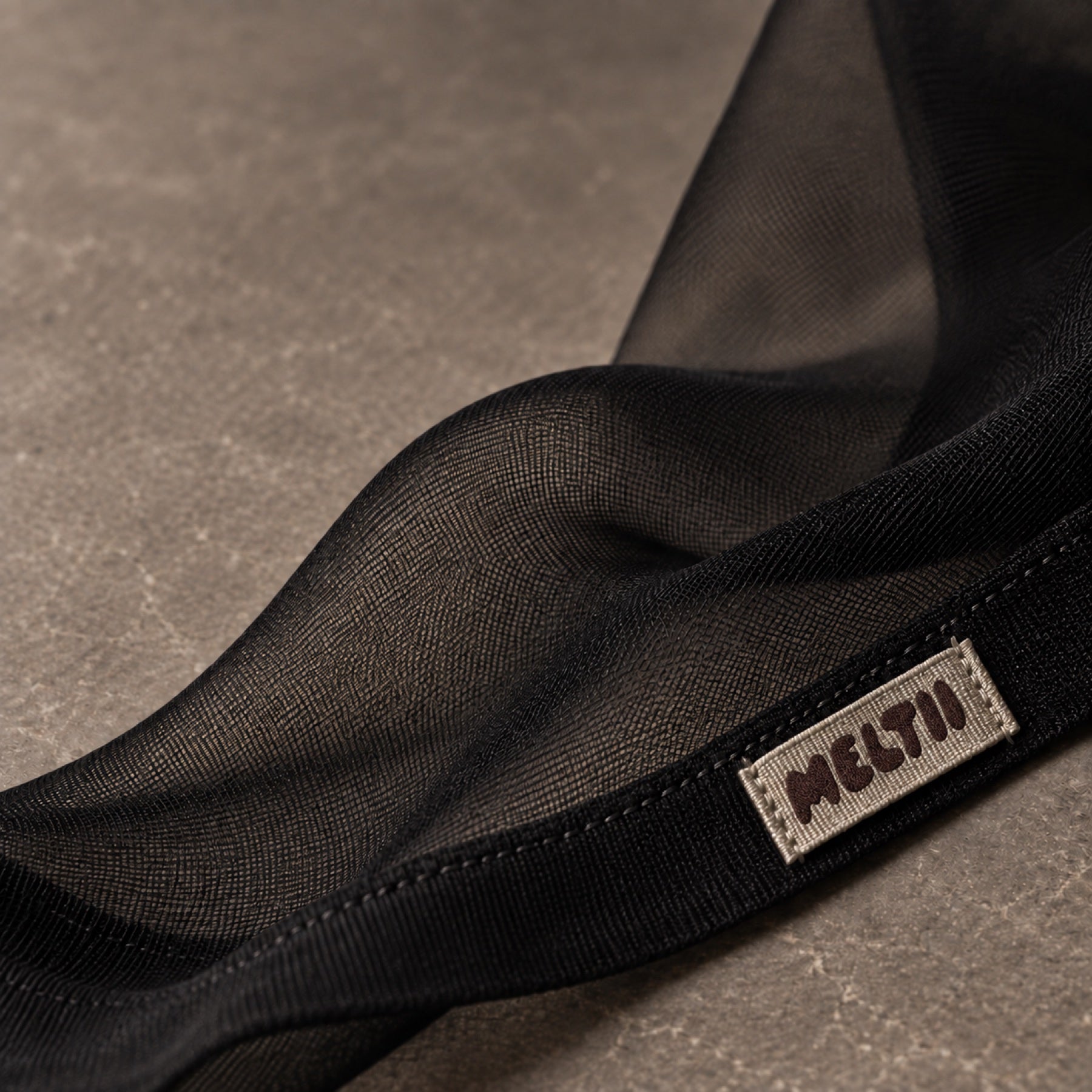 A woven Meltii label sewn into fine black hosiery.